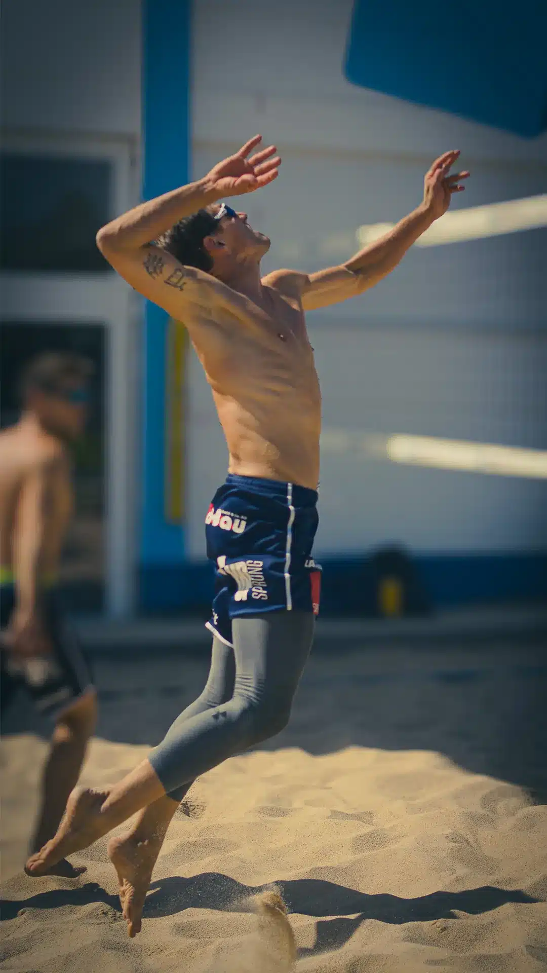 Beachvolleyballspieler beim kraftvollen Sprungaufschlag auf dem Sandfeld im Sportraum Mainz.