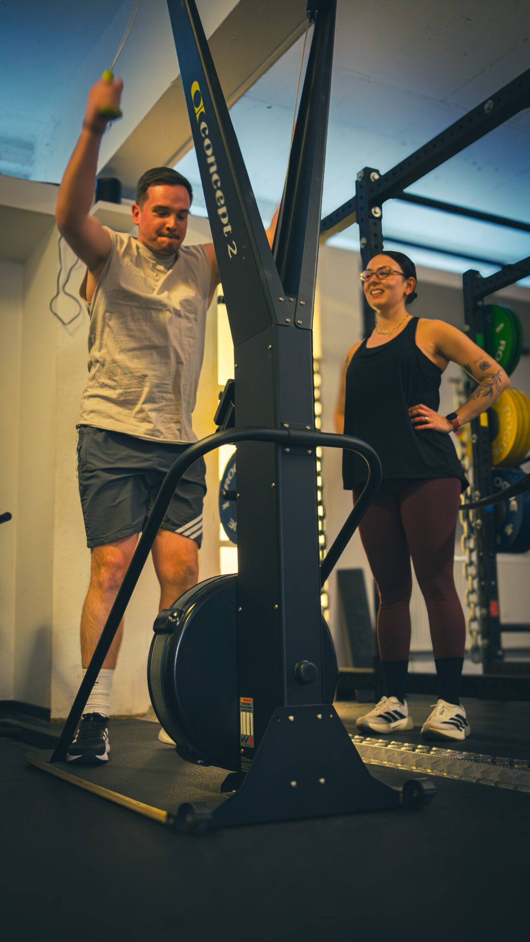 Ein Kursteilnehmer benutzt das Skiergometer und seine Freundin motiviert ihn 