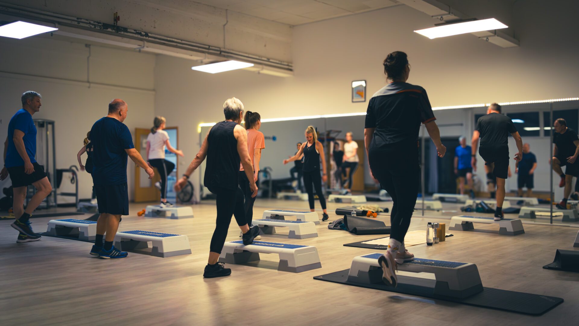 Gruppenteilnehmende steigen auf den Stepper auf und ab, für eine kurze Koordinationsübung